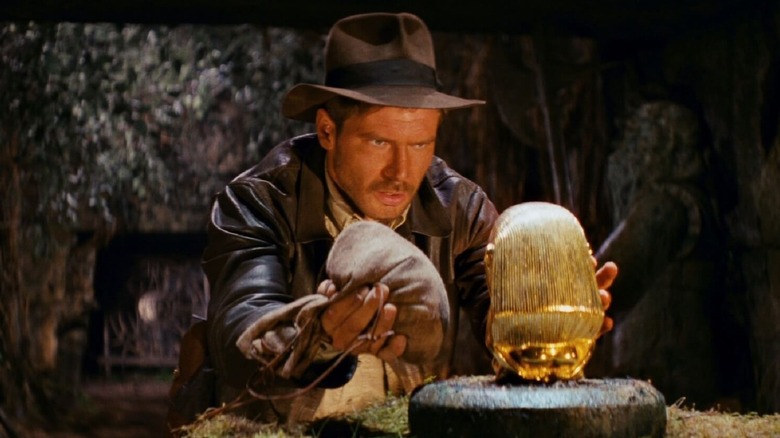 Indiana Jones weighs a bag of sand next to a golden idol 