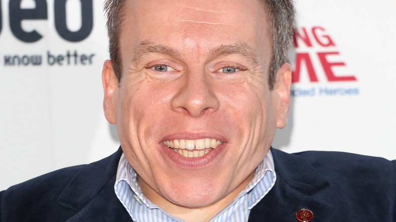 Warwick Davis smiling on red carpet