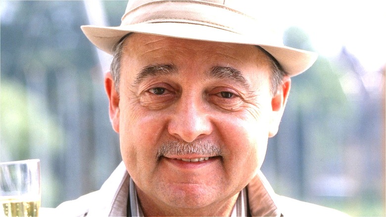 John Hillerman smiling while holding a drink and wearing a hat