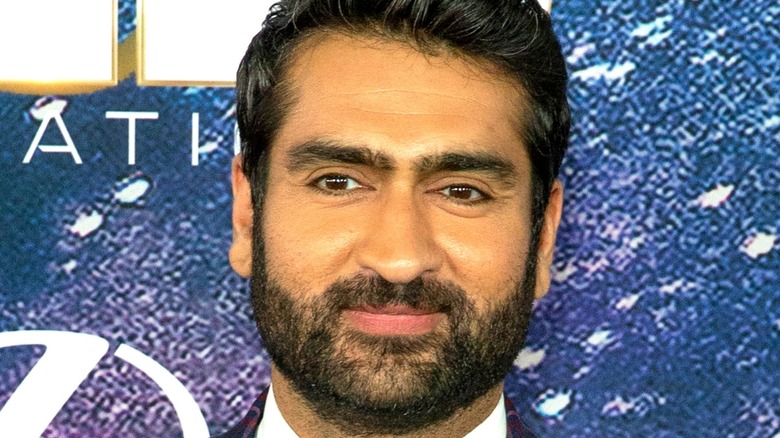Kamail Nanjiani smiling in front of purple background