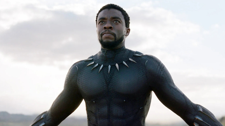 Black Panther stands unmasked with arms out in Black Panther.