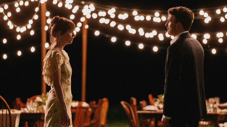 Lucy and John talk by outdoor dining tables and stringed lights at night in 