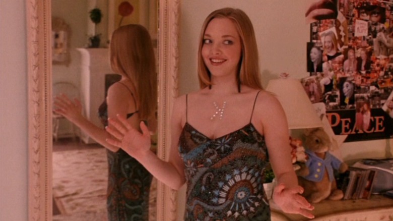 Karen stands in front of a mirror with a backwards K on her chest