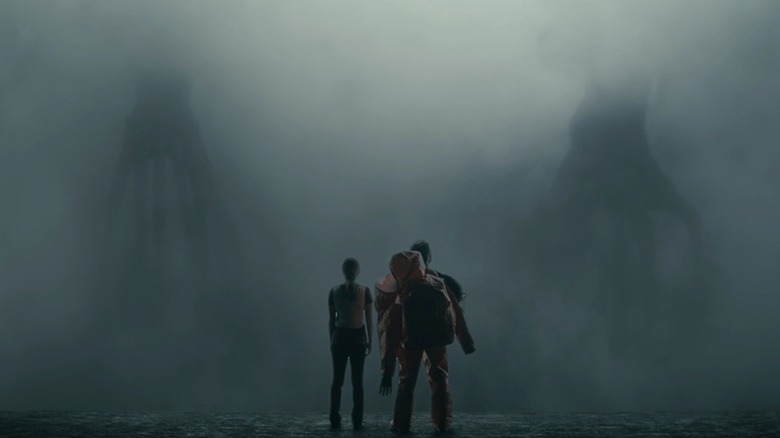 Louise and Ian standing before two fog-laden aliens who are separated from them by a translucent screen