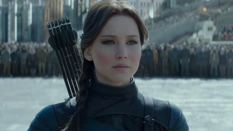 Katniss stands in black suit with arrows 