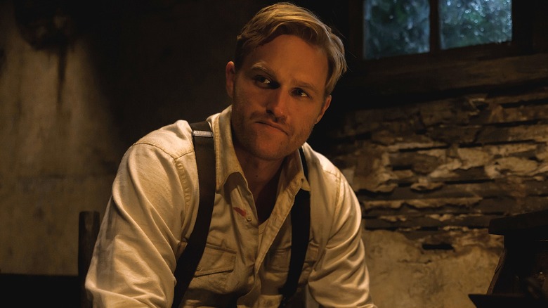 Lee Shaw wears a white shirt with suspenders in a dark basement in "Monarch"