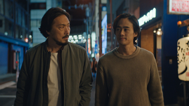 Kentaro looks over at his father Hiroshi as they walk down the streets of Tokyo in "Monarch"