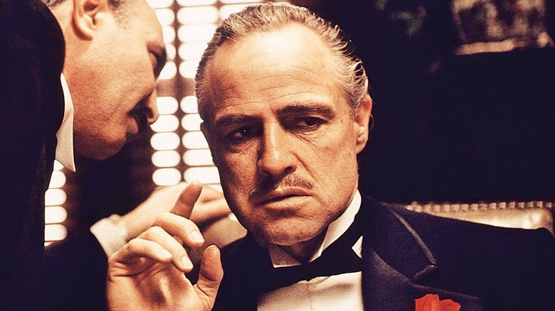 A man whispers in Vito Corleone's ear in 