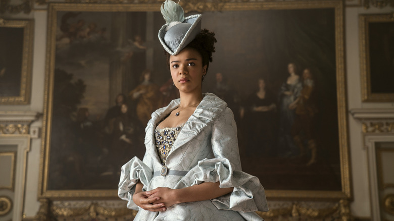 Queen Charlotte standing in a drawing room in a white gown and hat in Queen Charlotte: A Bridgerton Story (2023)