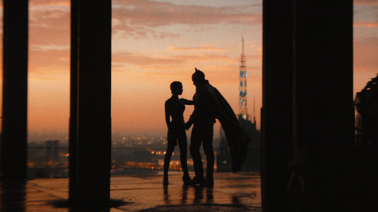 Catwoman and Batman standing closely in silhouette against a smoky, orange sunset