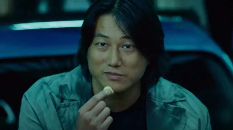 Han sits on the hood of a car and eats chips in "The Fast and the Furious: Tokyo Drift" (2006)
