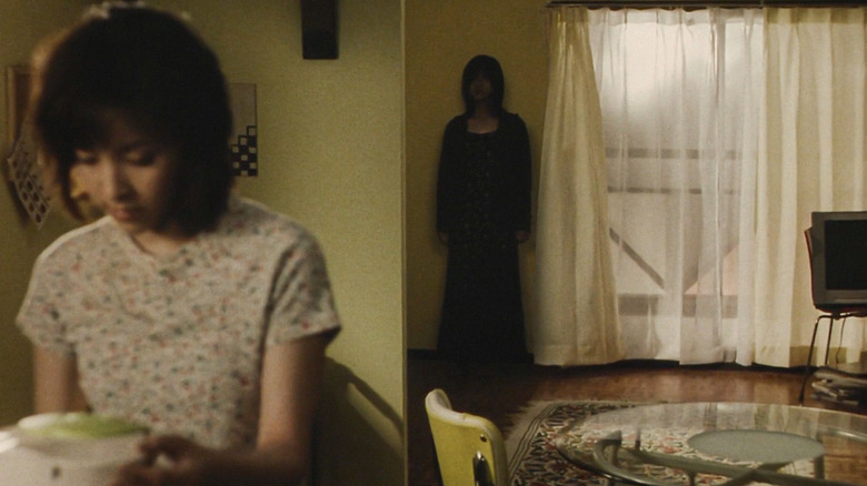 A shadowy figure stands against a wall as a women sits unaware in the foreground in "Pulse" (2001)