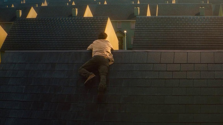 Tom climbs up onto the roof of a house in "Vivarium" (2019)