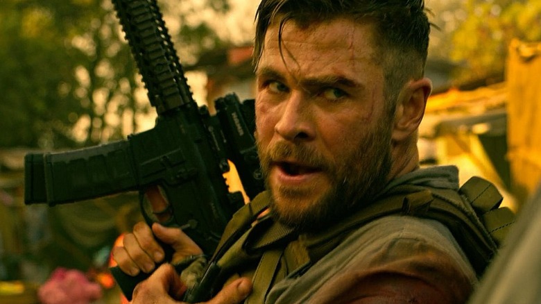 Tyler hides behind cover holding a machine gun in "Extraction" (2020)