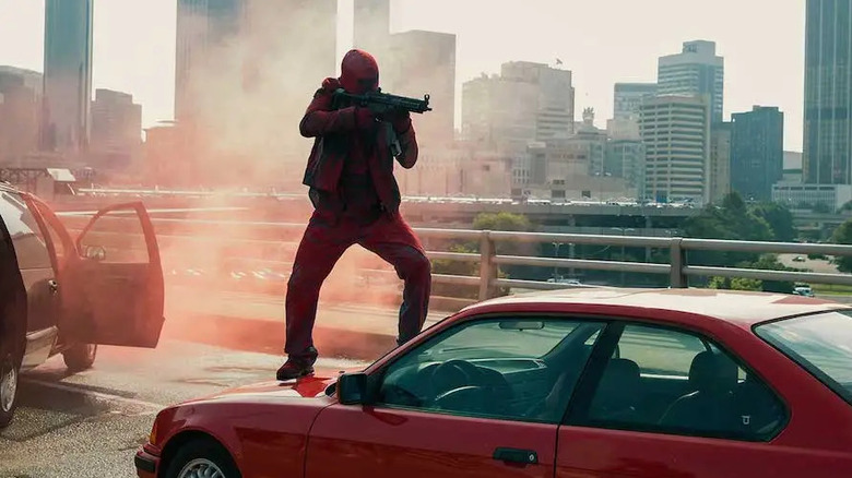 A masked gunman stands on a car and aims a machine gun in "Triple 9" (2016)