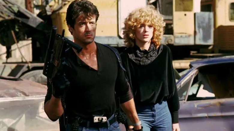 Cobra holding a submachine gun while wearing a tight black T-shirt and escorting Ingrid Knudsen in Cobra
