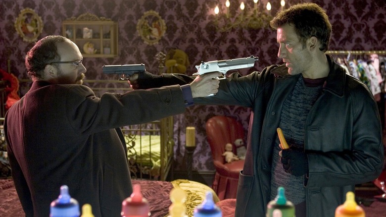 Smith and Hertz pointing guns at each other while Smith holds a carrot surrounded by baby bottles in Shoot 'Em Up