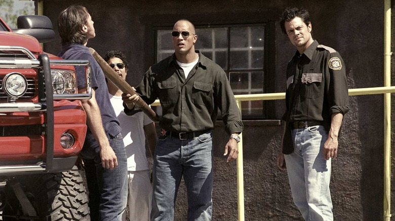 Chris Vaughn holding a 2x4 up to a man he's trying to intimidate while Ray slouches next to him in Walking Tall