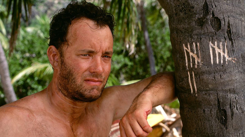 Chuck standing next to a tree with notches in it in Cast Away