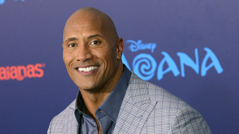 Dwayne Johnson smiling with a "Moana" logo behind him