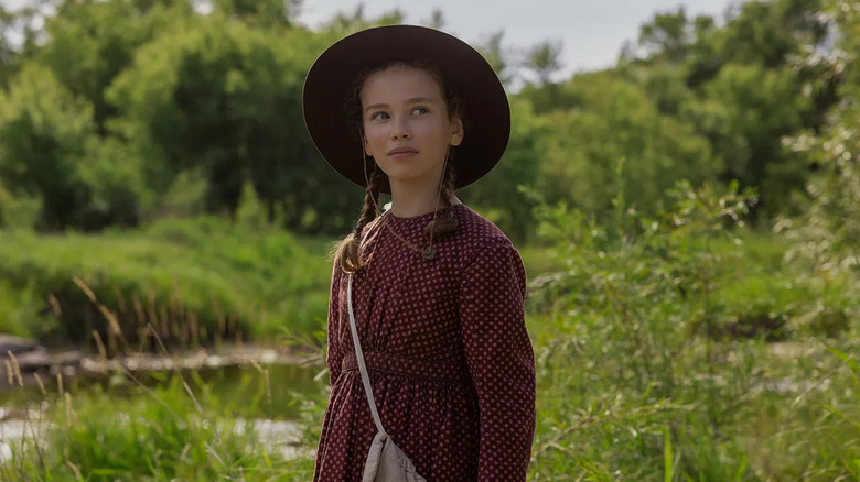 Laura wearing a hat in a field looking at something on Little House on the Prairie