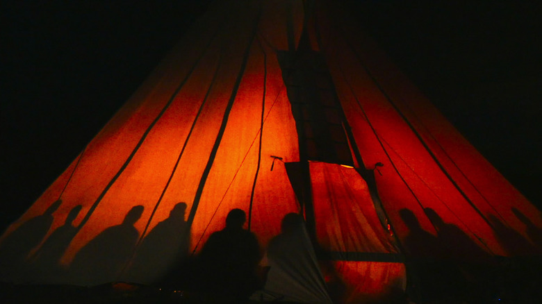 Silhouettes of people inside a lit tent at night in How to Change Your Mind (2022)