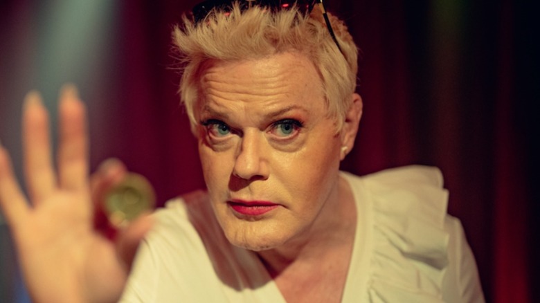 Lachy holds up a token in "Kaos" (2024)