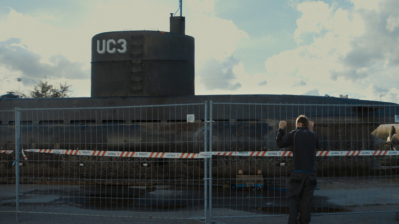 A man holding onto a fence, looking at a submarine, in "Into the Deep: The Submarine Murder Case"
