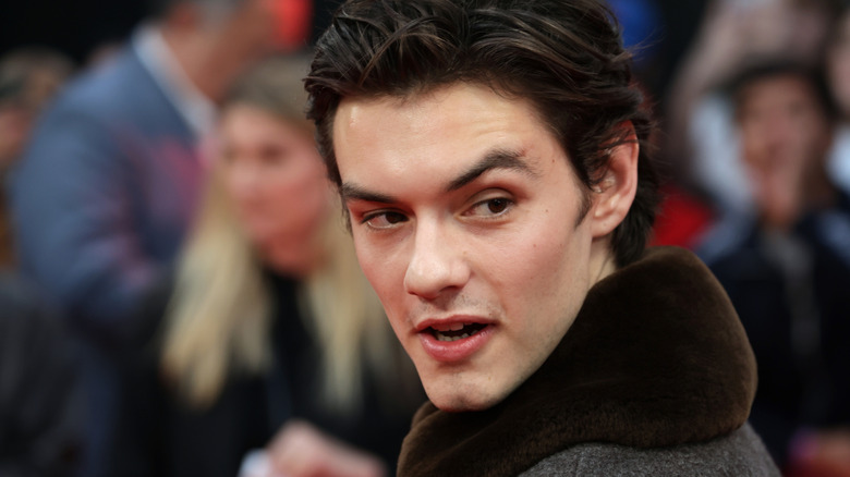 Close-up shot of Louis Partridge dressed in a jacket with a large, velvet-trim collar at the premiere of "Jay Kelly"