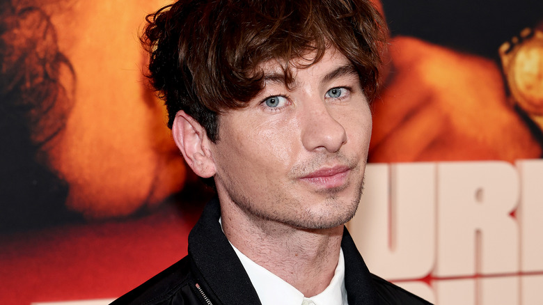 Close-up shot of actor Barry Keoghan posing in front of a movie poster and white block letters at a carpet premiere event