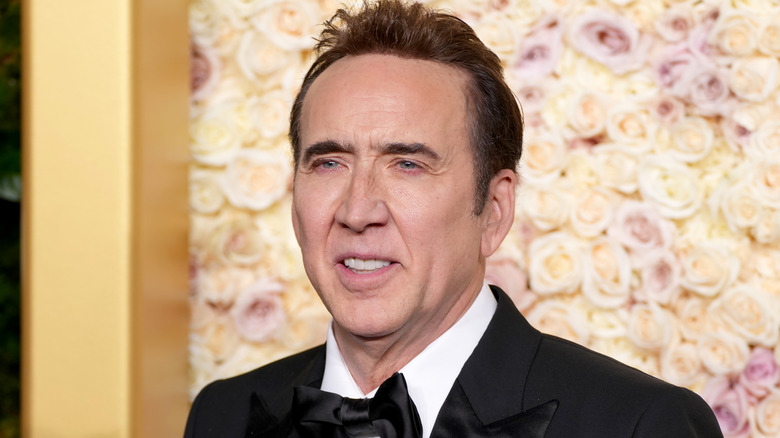 Nicolas Cage smiling in a tux with flowers in the background