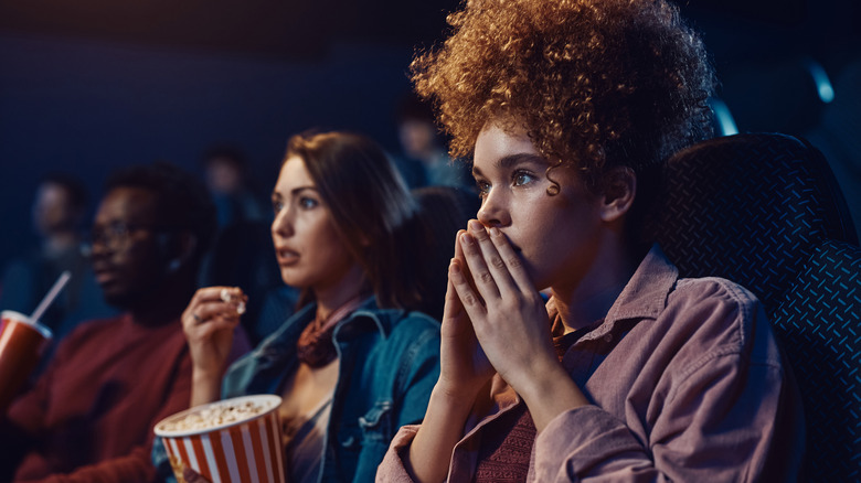 Three friends watching a scary movie in a theater
