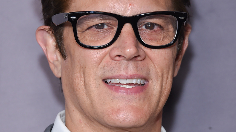 Johnny Knoxville wearing glasses against a grey background