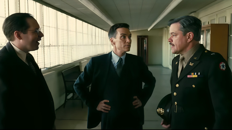 Robert Oppenheimer speaks with a scientist and Leslie Groves in Oppenheimer