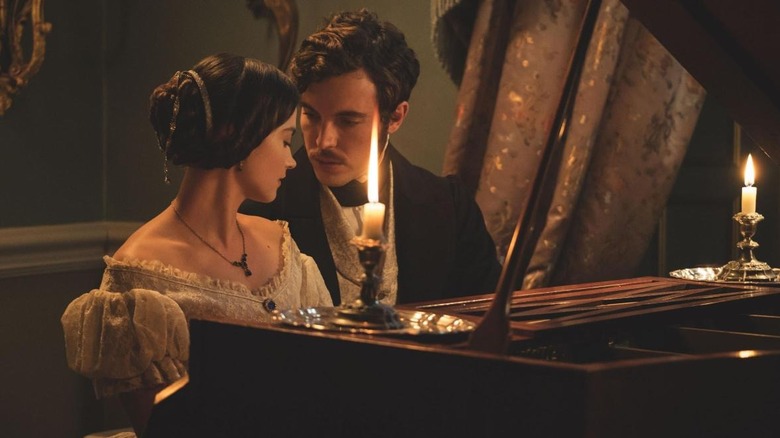 Victoria and Albert sitting together closely on a piano bench making intimate eye contact by candlelight