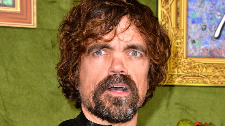 Peter Dinklage poses in front of a green backdrop