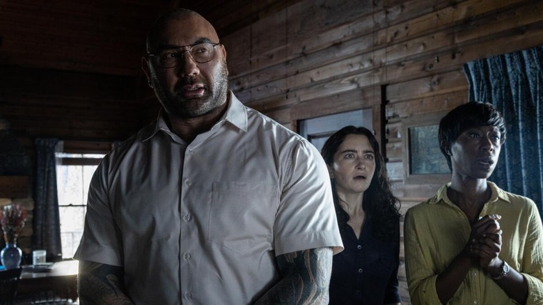 Leonard, Sabrina, and Adriane look surprised standing in the cabin in A Knock at the Cabin (2023)