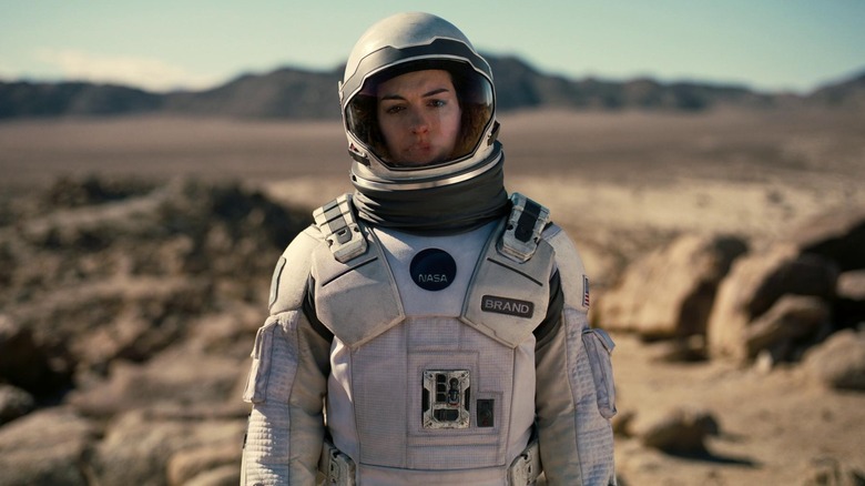 Brand stands on a rocky planet in a spacesuit, calmly looking into the distance in Interstellar (2014)