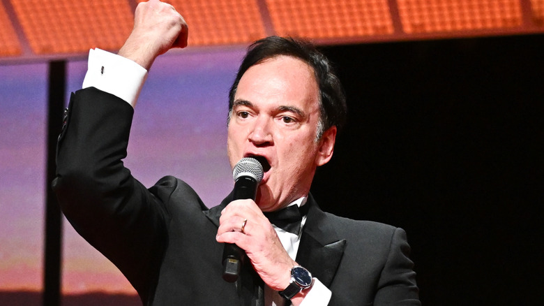 Quentin Tarantino speaking into a microphone with his other fist in the air