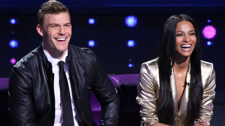 Alan Ritchson and Ciara smiling on a couch in "I Can Do That"