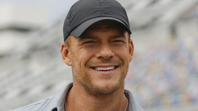 Alan Ritchson smiling at the NASCAR Cup Series Daytona 500 in 2025 in Daytona Beach, Florida.