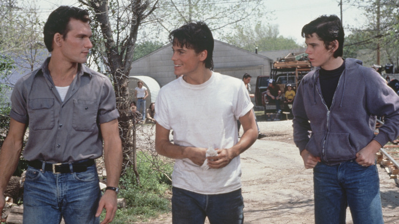 Patrick Swayze, Rob Lowe, and C. Thomas Howell walking on the set of The Outsiders