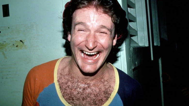 Robin Williams grinning, mid-laugh, in 1980 in a low-cut shirt