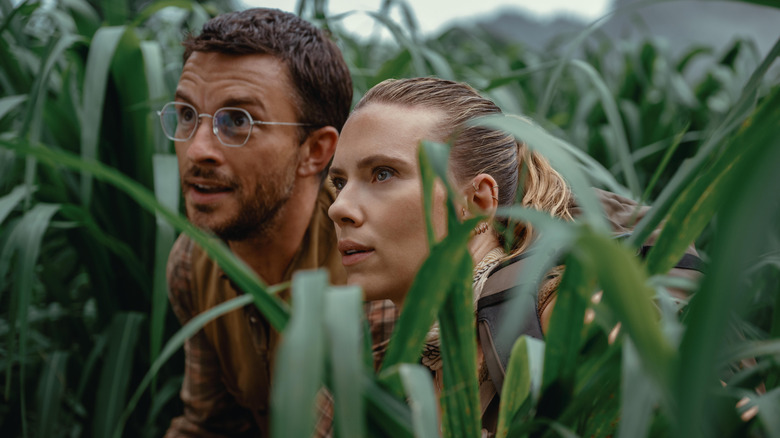 Henry and Zora hiding in the grass in "Jurassic World Rebirth" (2025)