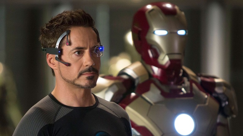 Tony Stark wears a headset next to an Iron Man suit in "Iron Man 3" (2013)