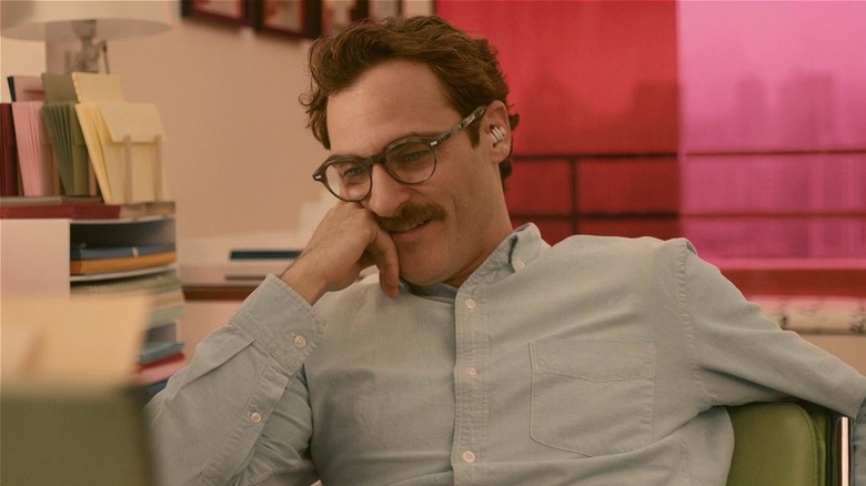 Theodore Twombly smiling at desk with earbud in on Her