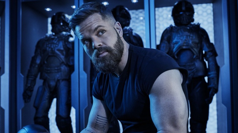 Amos sitting in front of some exosuits in The Expanse