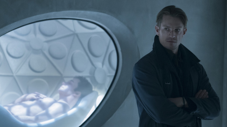 Takeshi Kovacs standing with his arms crossed in front of a window in Altered Carbon