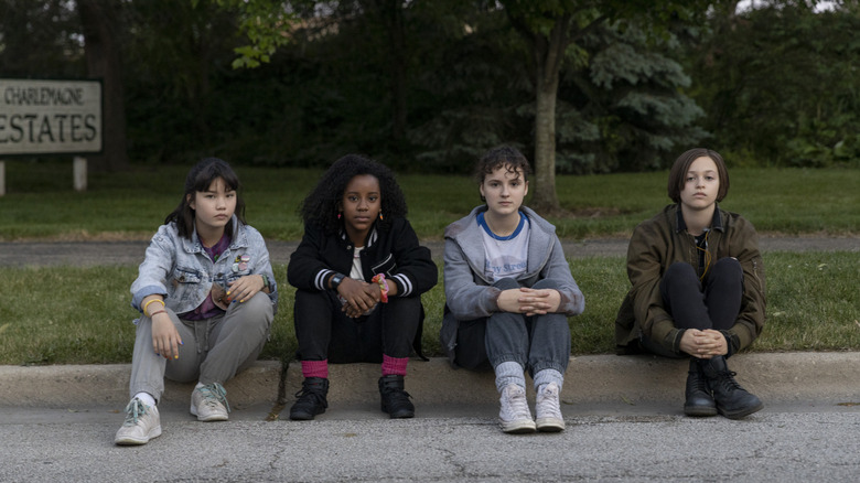 Erin, Tiffany, KJ, and Mac sitting on a curb in "Paper Girls"