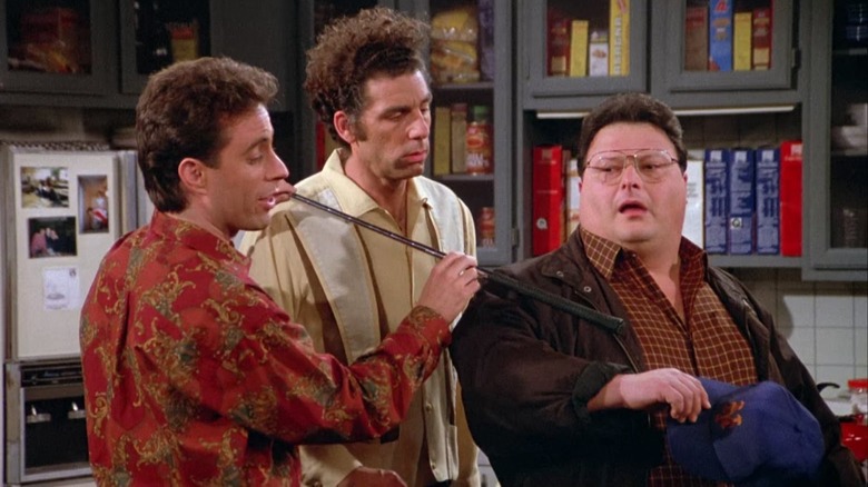 Jerry indicating Newman's wrist with a golf club while Kramer looks on